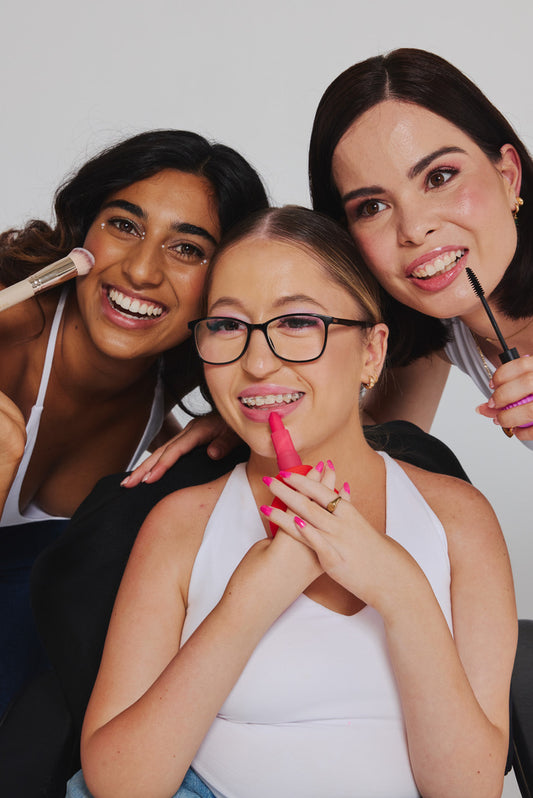 Three women together, one applying lip colour with a pink ByStorm grip while the others hold ByStorm makeup tools