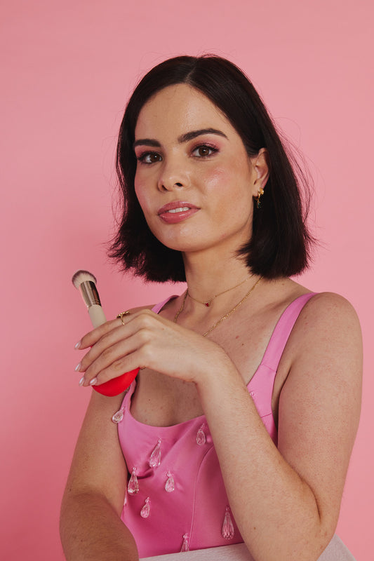 A woman holding a coral ByStorm makeup grip near her lips