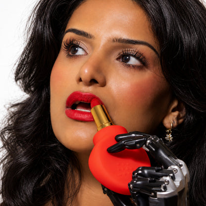 Woman applying red lipstick held in a red ByStorm Margie grip, using a bionic prosthetic hand