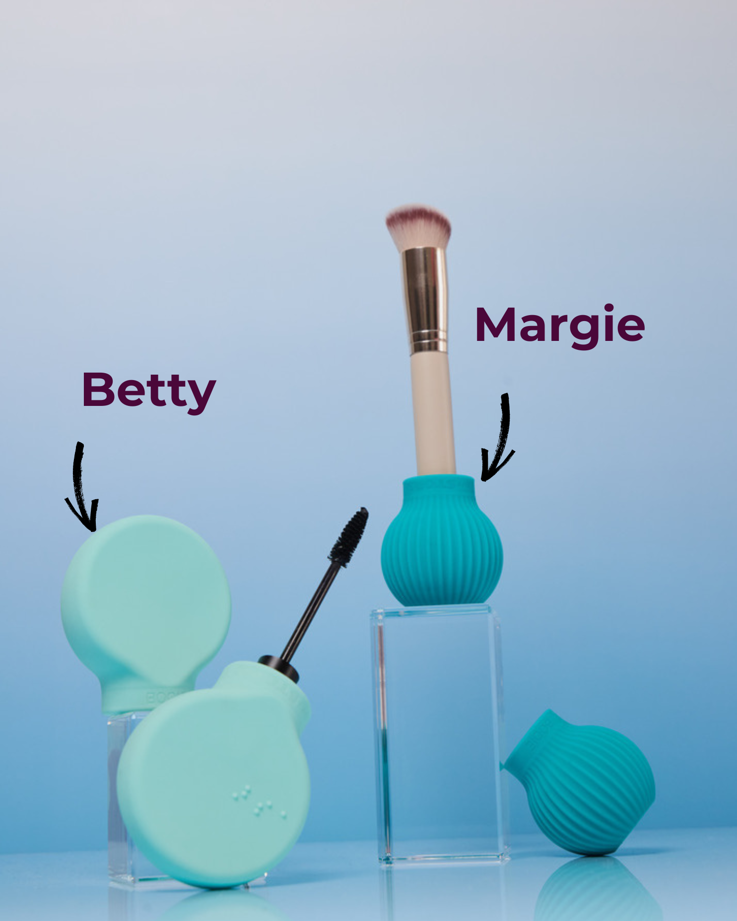 Two adaptive beauty tools displayed against a gradient blue background. On the left is 'Betty', a flat, circular turquoise grip attached to a mascara wand. On the right is 'Margie', a ribbed, spherical turquoise grip holding a makeup brush upright. Both products have their names labelled with arrows pointing to them