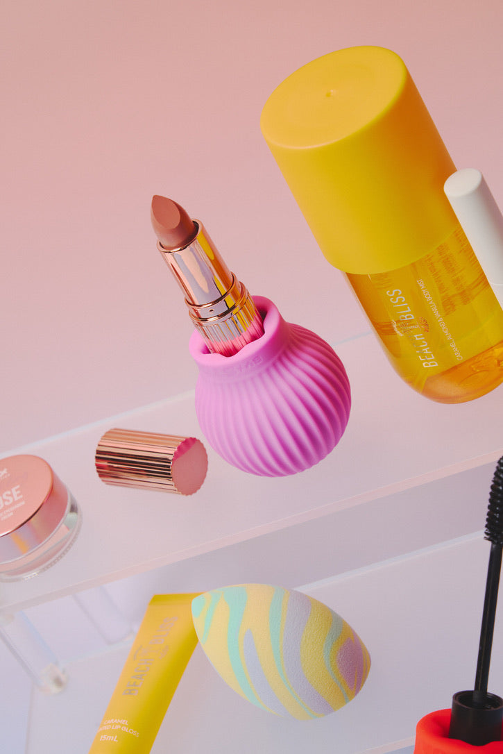 Betty, a pink ball-shaped adaptive grip holds a lipstick surrounded by other makeup items. 
