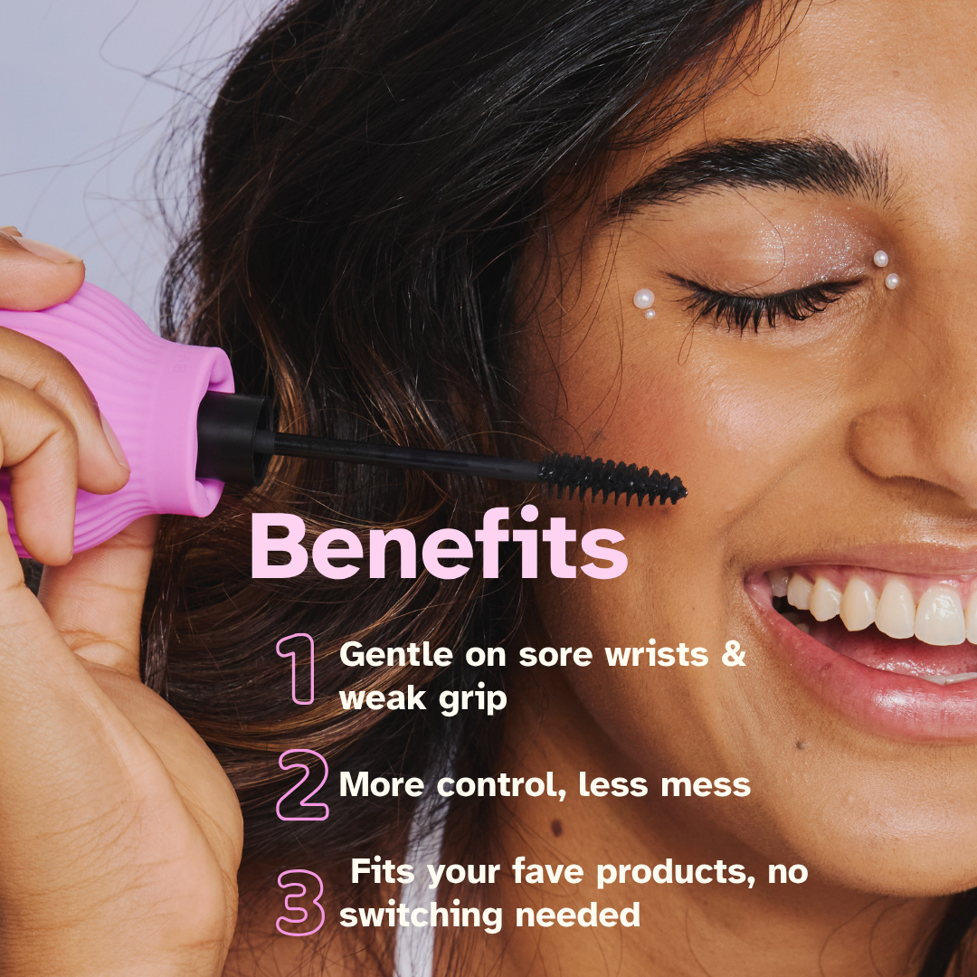 A smiling person uses ByStorm’s Betty, a pink-handled, disability-friendly mascara tool. Benefits: gentle on sore wrists, offers more control with less mess, and works with your favorite products so no need to switch.