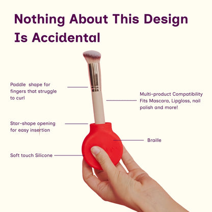 A hand holds a red and beige makeup brush with callout lines and text explaining its design features, including paddle shape, star-shaped opening, soft touch silicone, and multi-product compatibility, on a cream background.