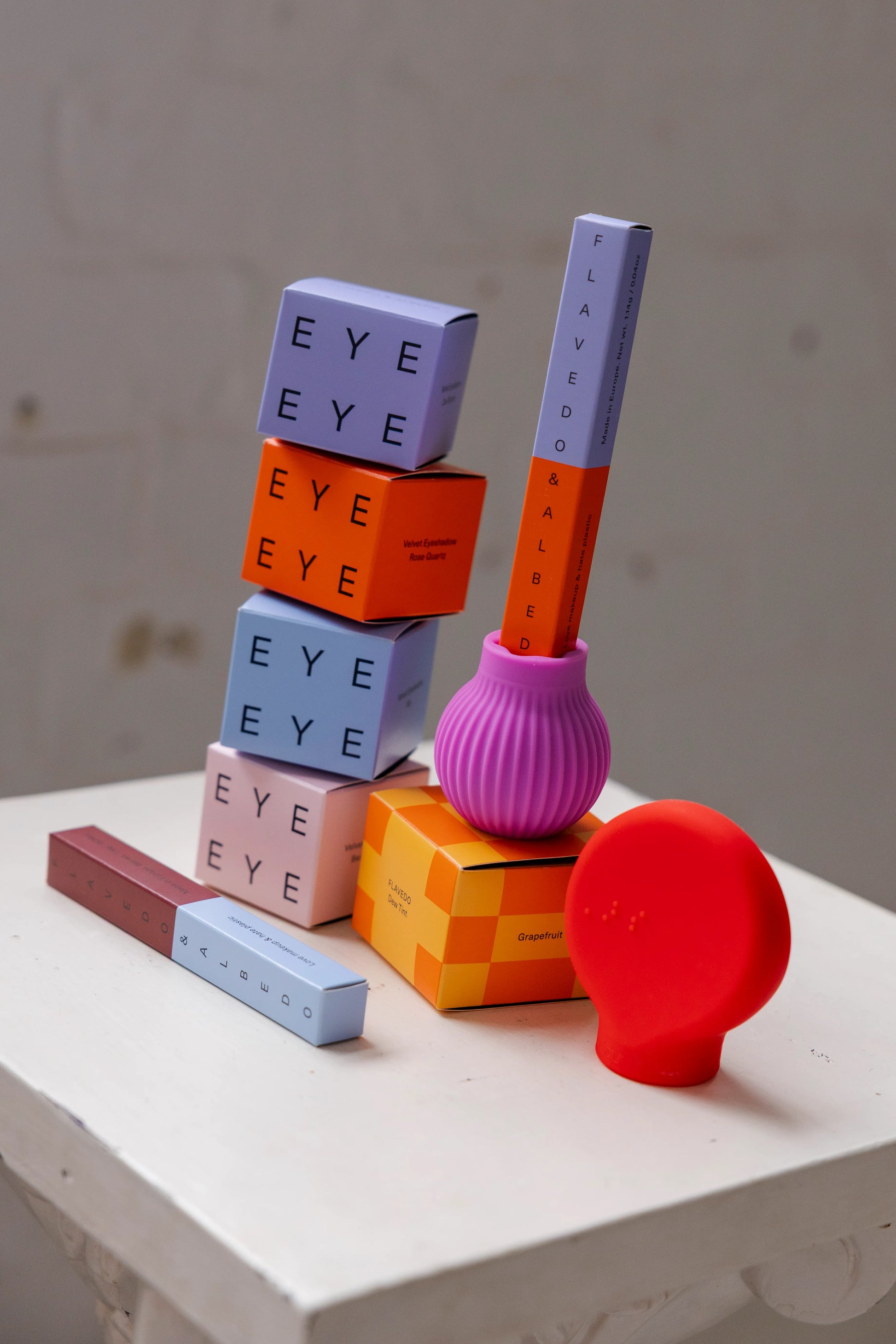 Colorful cosmetics stacked creatively on a white surface. Includes eye blocks, lipsticks , and brush accessories attached to ByStorm grip tool with a playful, artistic vibe.
