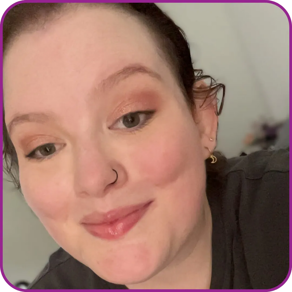 Close-up of a person with makeup, wearing earrings, against a neutral background.