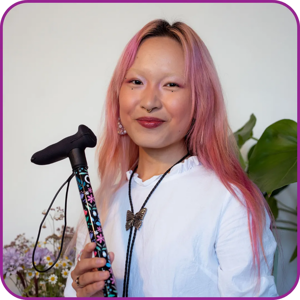 Person with pink hair holding a colorful walking stick against a light background