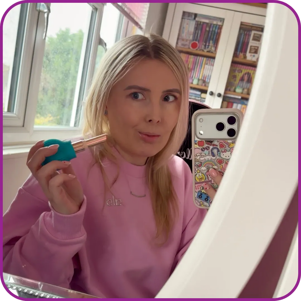 Person in a pink sweatshirt holding a phone with a colorful case, sitting indoors.