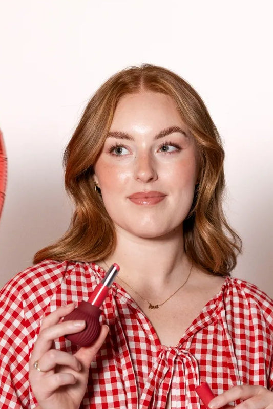 Woman holding an adaptive mauve ball-shaped makeup grip with lipstick, designed for easier makeup application and improved control.