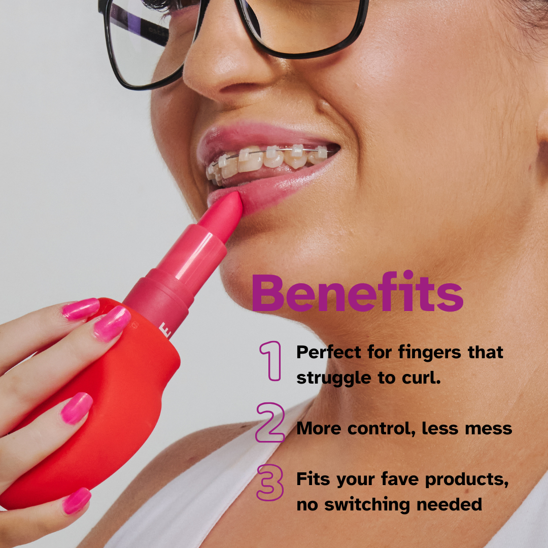 A woman with glasses applies lipstick using Margie by ByStorm, a red ergonomic beauty tool. Benefits: ideal for fingers that struggle to curl, offers more control and less mess, fits your favorite products—an adaptive makeup grip.