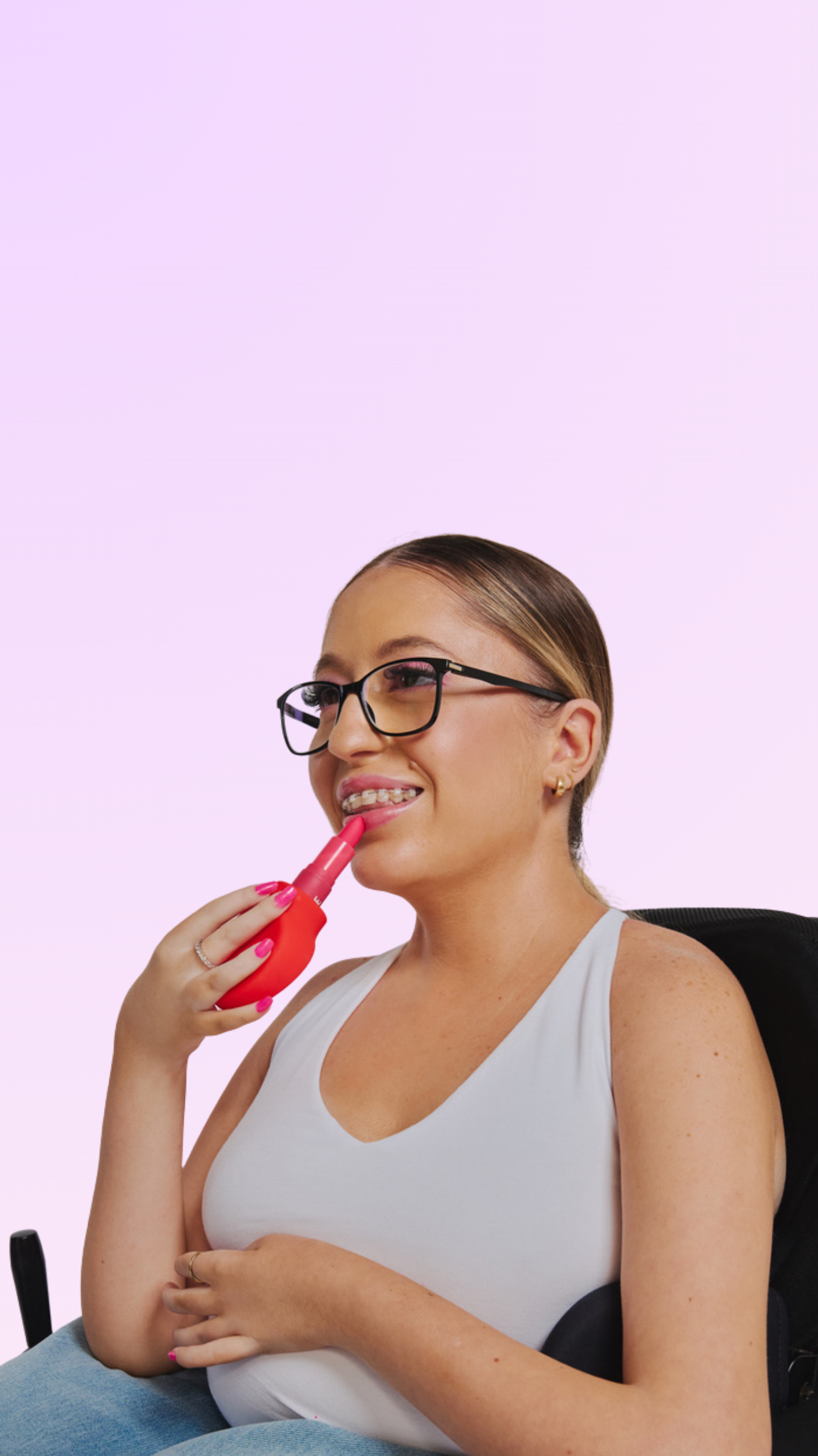 a disabled women in a wheelchair holds margie, a paddle shape makeup accessory with lipstick up to her lips. 