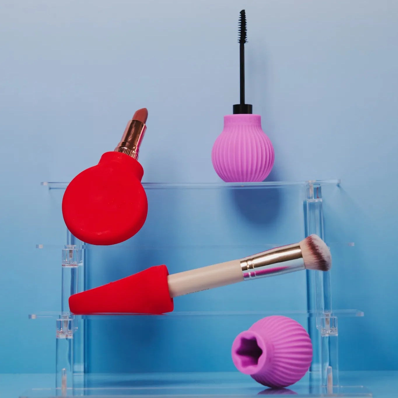 Accessible beaut tools -  Betty a pink ball-shape and margie a red paddle shape, items on a clear acrylic stand against a blue gradient background