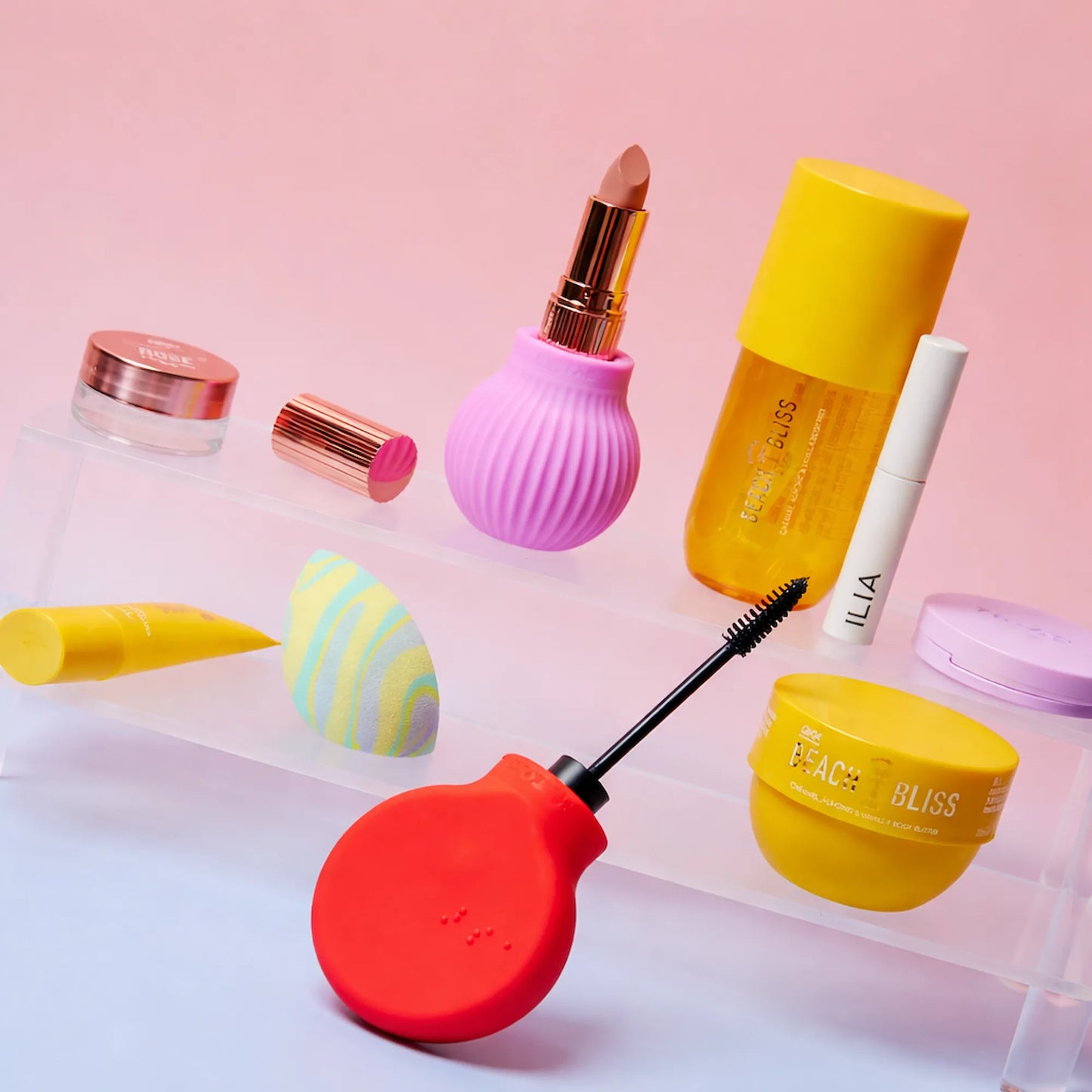 ByStorm Betty pink and Margie red adaptive makeup grip tools surrounded by compatible beauty products on acrylic display shelves