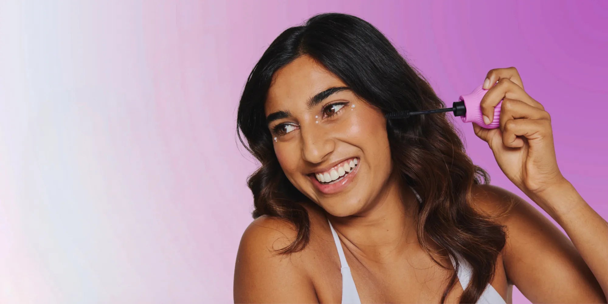 Woman holding Betty, a pink ball-shaped adaptive makeup grip by ByStorm with mascara attached for easier application