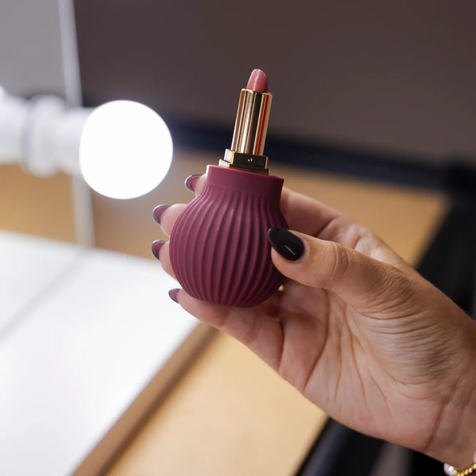 Woman holding Betty, a mauve ball-shaped adaptive makeup grip by ByStorm with lipstick attached for easier application