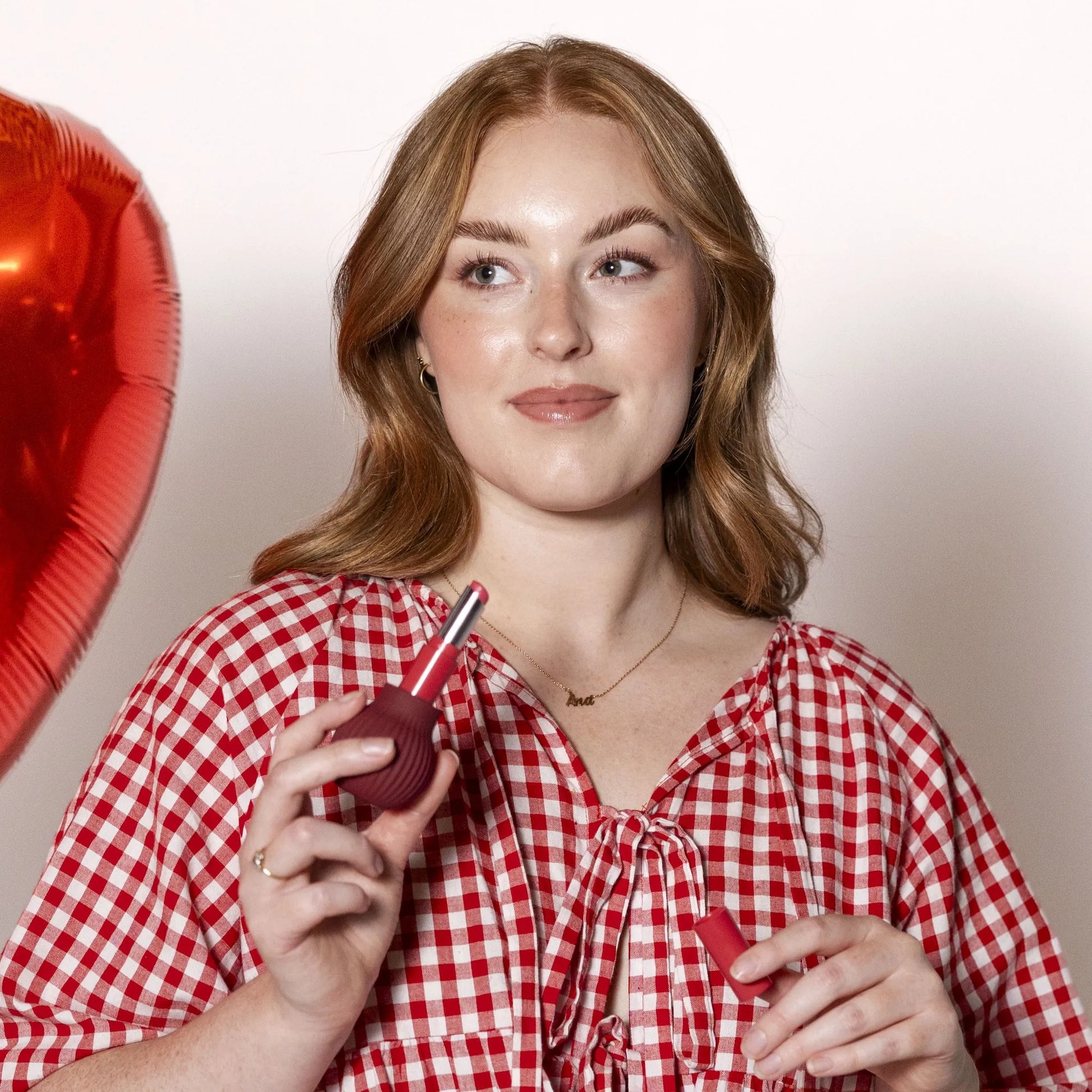 Woman holding Betty, a mauve ball-shaped adaptive makeup grip by ByStorm with lipstick attached for easier application