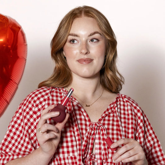 Woman holding Betty, a mauve ball-shaped adaptive makeup grip by ByStorm with lipstick attached for easier application