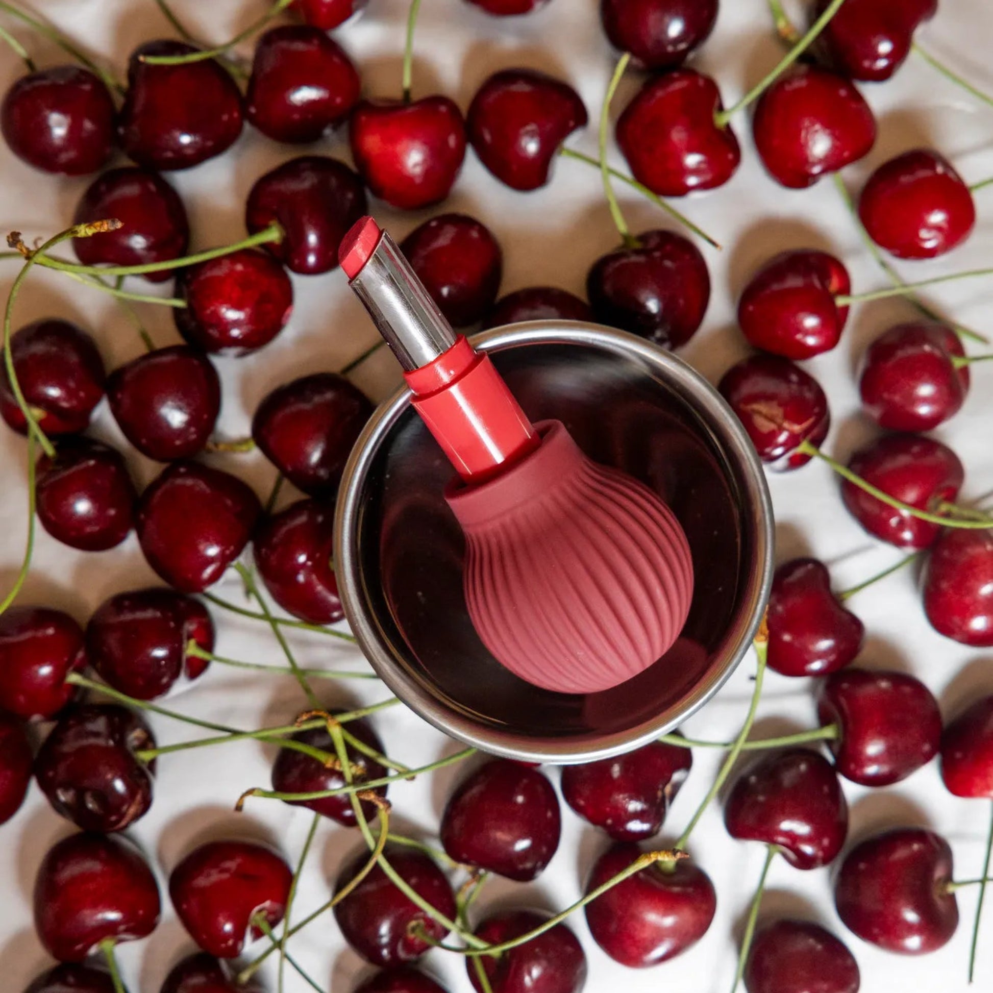 Betty, a mauve ball-shaped accessible makeup tool by ByStorm, holding a lipstick on a white background