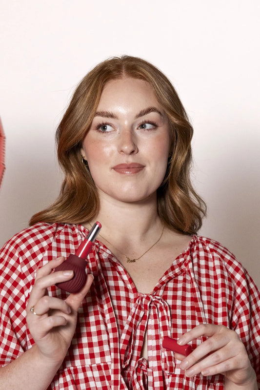 Woman holding Betty, a mauve ball-shaped adaptive makeup grip by ByStorm with lipstick attached for easier application