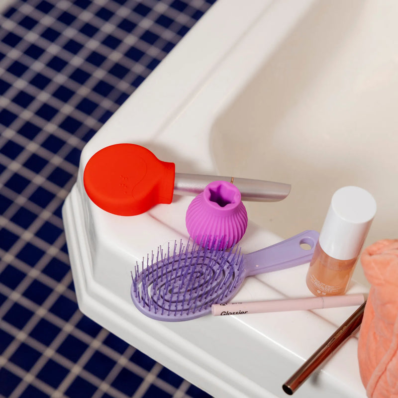 ByStorm Betty and Margie, makeup grip adaptive tools on bathroom sink flatlay, with Margie holding mascara.