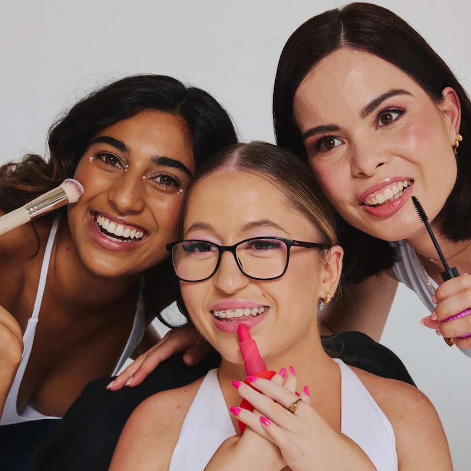 Three women smiling while holding cosmetics attached to a ByStorm adaptive grip tool.