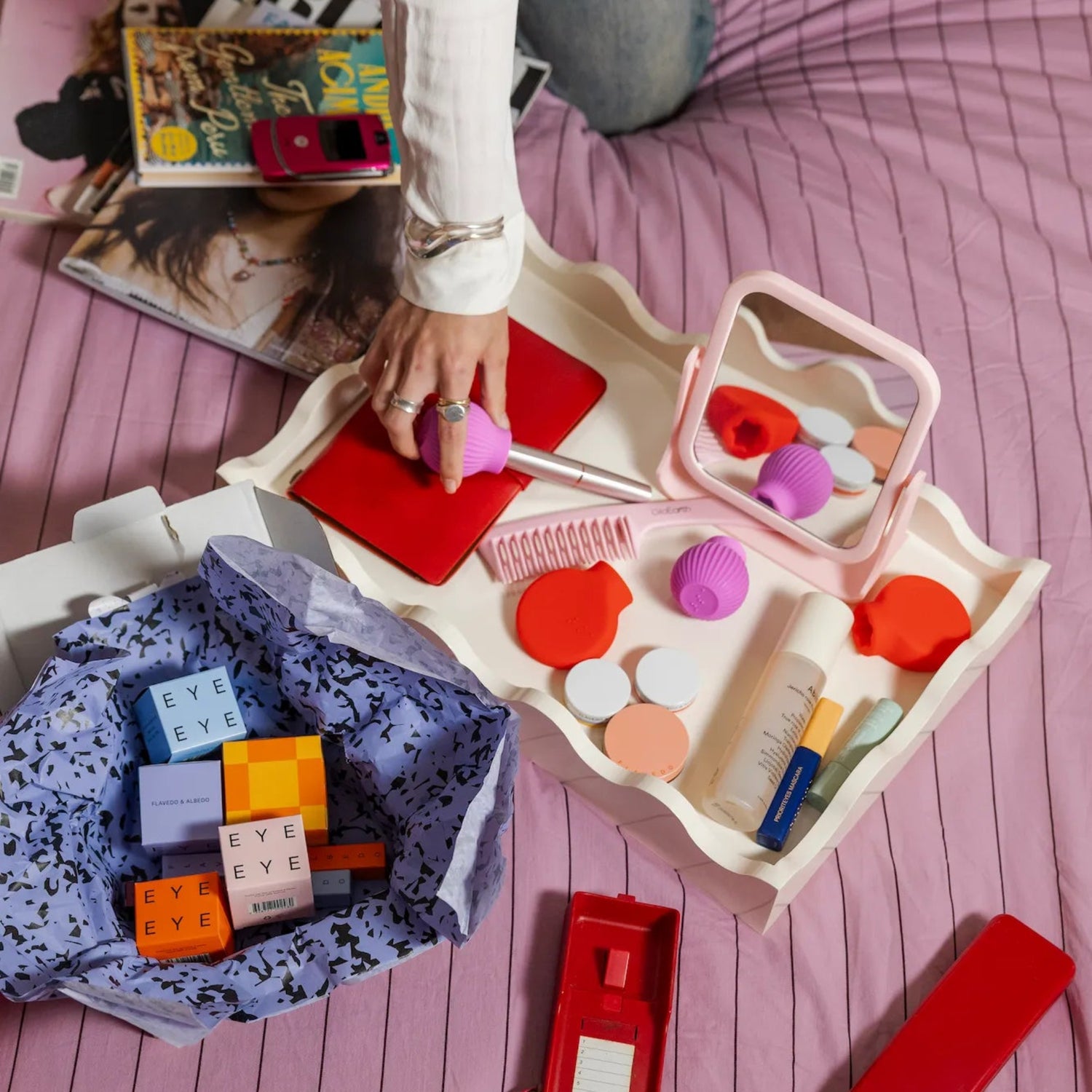 Flatlay of ByStorm adaptive makeup grip tool with cosmetics on a tray, and a hand holding mascara attached to a ByStorm adapative makeup grip tool.