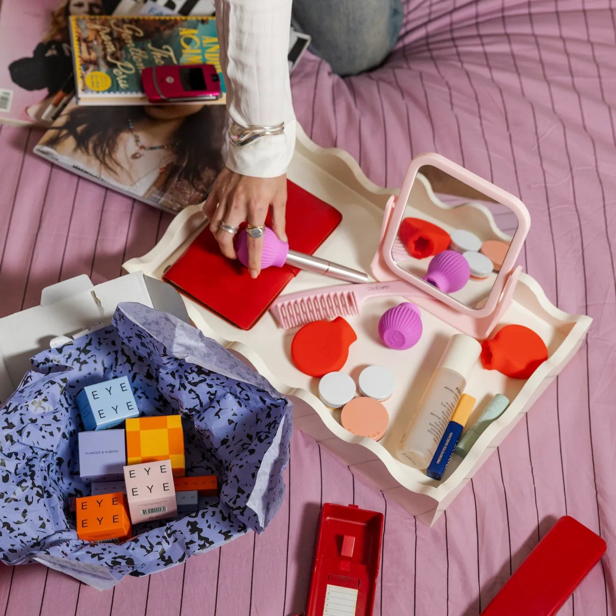 Flatlay of ByStorm adaptive makeup grip tool with cosmetics on a tray, and a hand holding mascara attached to a ByStorm adapative makeup grip tool.