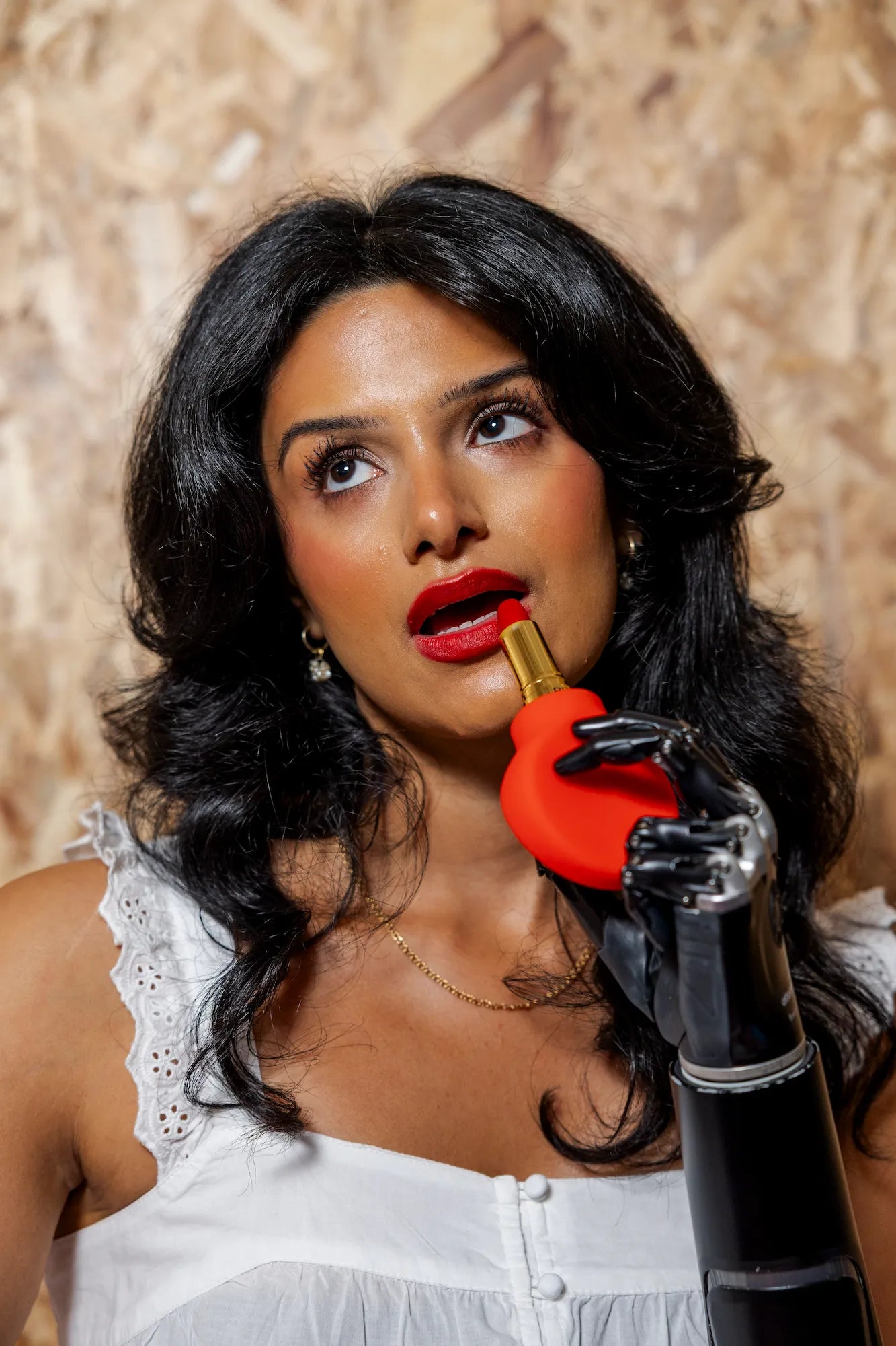 Woman with a bionic arm applying lipstick using Margie, a red paddle-shaped accessible makeup tool by ByStorm.