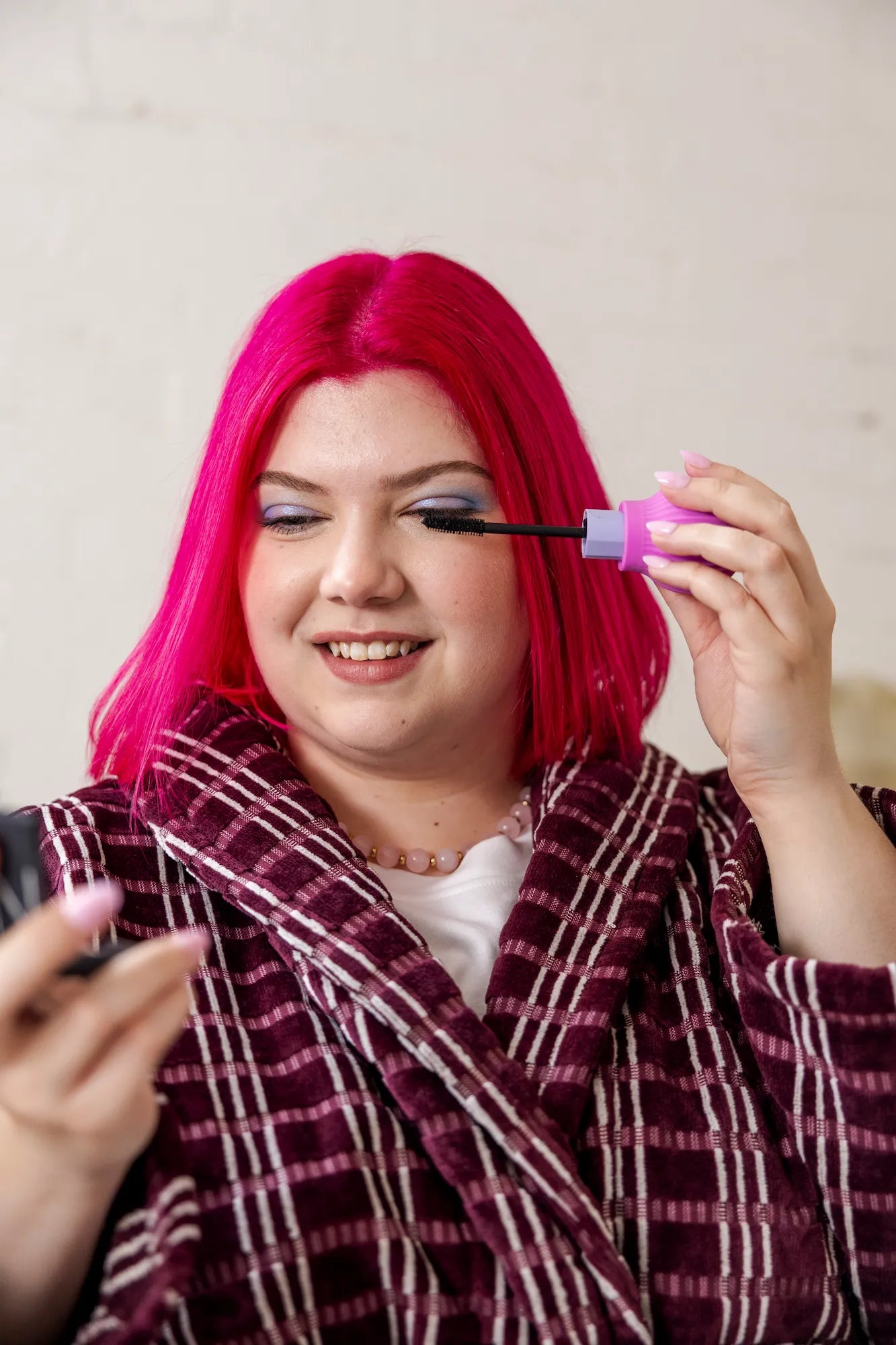 Woman smiling while applying mascara using a ByStorm adaptive makeup grip tool during her morning routine