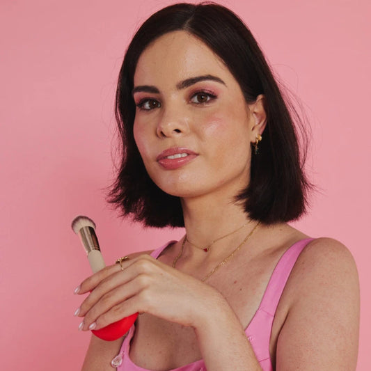 Woman holding a makeup product against a pink background