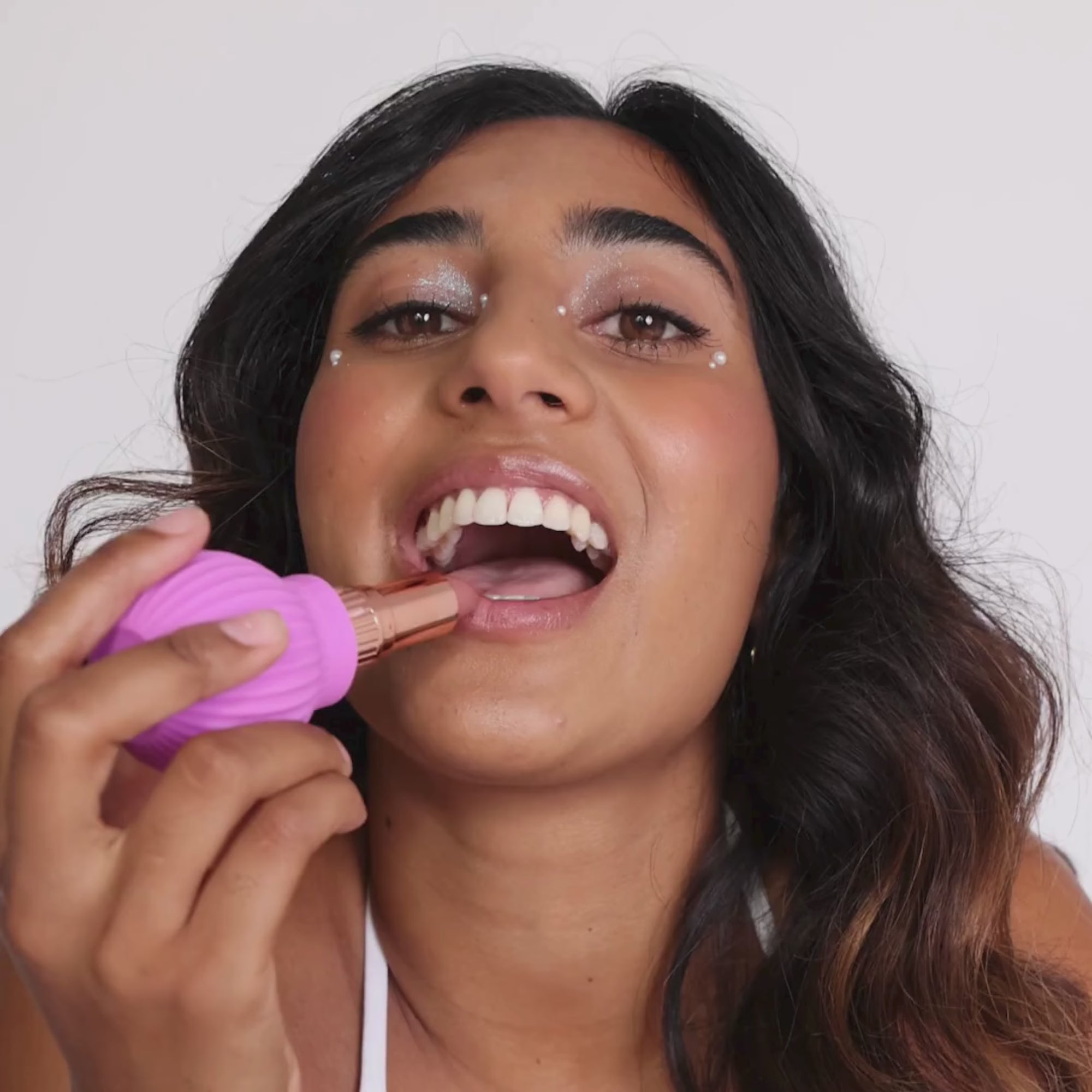 Woman holding Betty, a pink ball-shaped adaptive makeup grip by ByStorm with lipstick attached for easier application