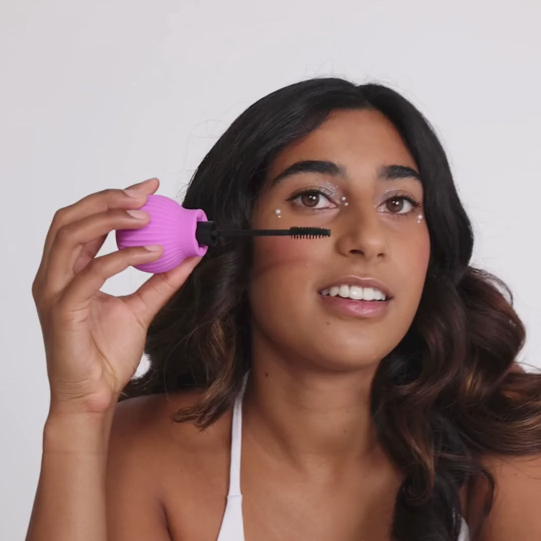 Woman holding Betty, a pink ball-shaped adaptive makeup grip by ByStorm with lipstick attached for easier application