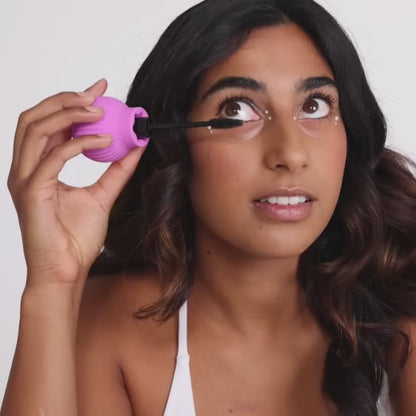 Woman holding Betty, a pink ball-shaped adaptive makeup grip by ByStorm with mascara attached for easier application