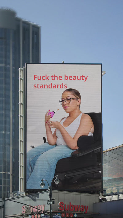 Billboard Ad, with words "Fuck the beauty standards" and a woman in a wheelchair holding ByStorm Beauty Betty pink ball-shaped adaptive makeup tool